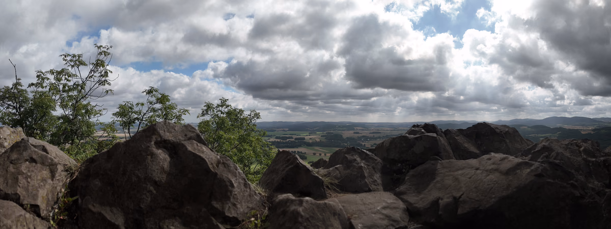 Panorama Krainy Wygasłych Wulkanów widoczna ze szczytu Ostrzycy z bazaltowymi skałami na pierwszym planie.